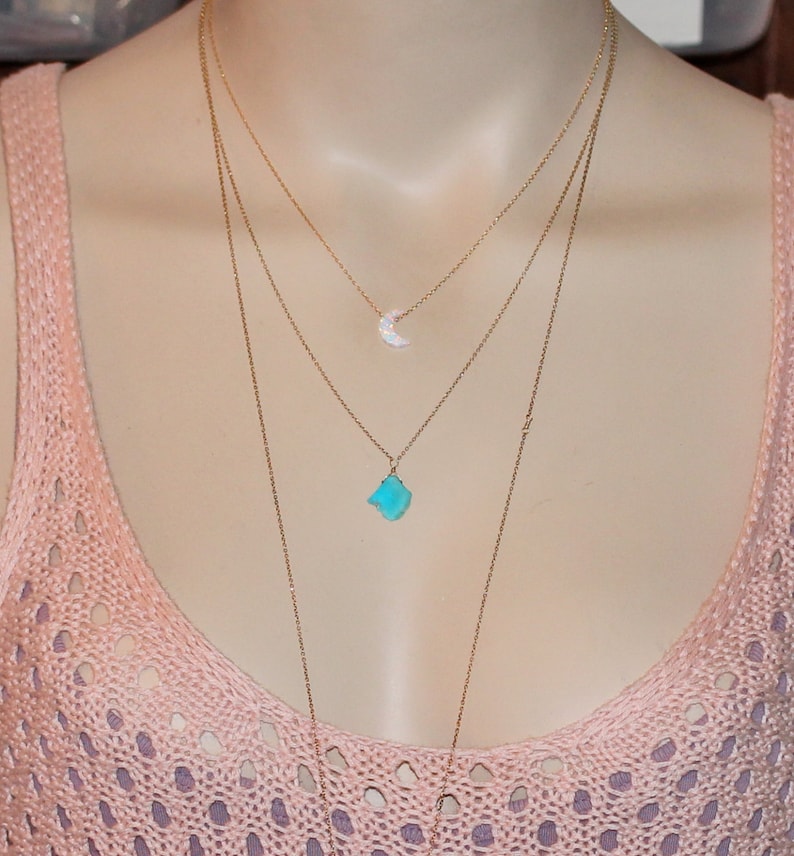 May include: A layered gold necklace with a turquoise stone pendant and a small crescent moon pendant.