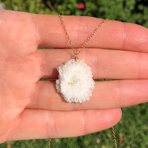 May include: A gold chain necklace with a white crystal pendant. The crystal is a cluster of small, white crystals.