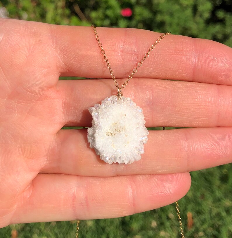 May include: A gold chain necklace with a white crystal pendant. The crystal is a cluster of small, white crystals.