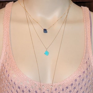May include: A layered gold necklace with two turquoise and blue gemstone pendants.