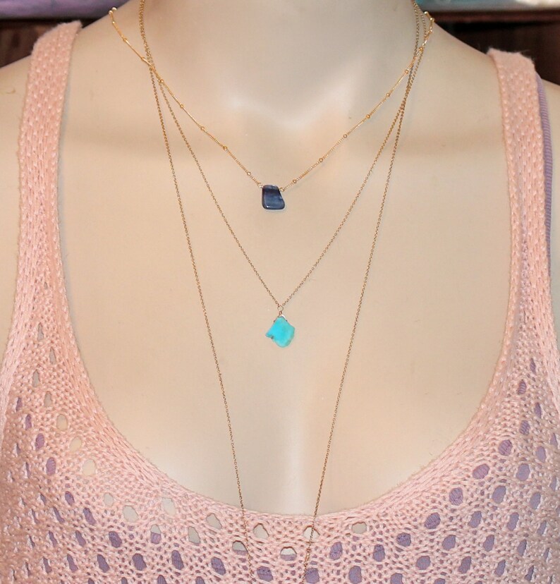 May include: A layered gold necklace with two turquoise and blue gemstone pendants.