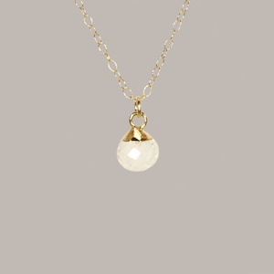 May include: A delicate gold chain necklace with a small, white, faceted gemstone pendant.