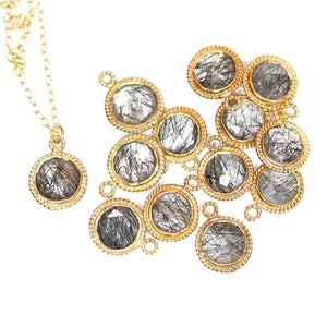 May include: A gold chain necklace with a pendant featuring a round, clear quartz stone with black inclusions. The pendant is surrounded by a gold rope-like border. There are several similar pendants scattered around the necklace.