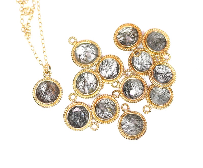 May include: A gold chain necklace with a pendant featuring a round, clear quartz stone with black inclusions. The pendant is surrounded by a gold rope-like border. There are several similar pendants scattered around the necklace.