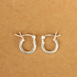 May include: A pair of silver hoop earrings. The earrings are small and simple, with a smooth, polished finish.