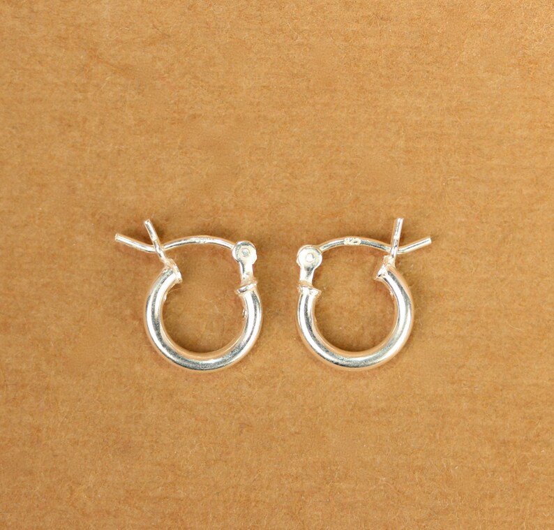 May include: A pair of silver hoop earrings. The earrings are small and simple, with a smooth, polished finish.