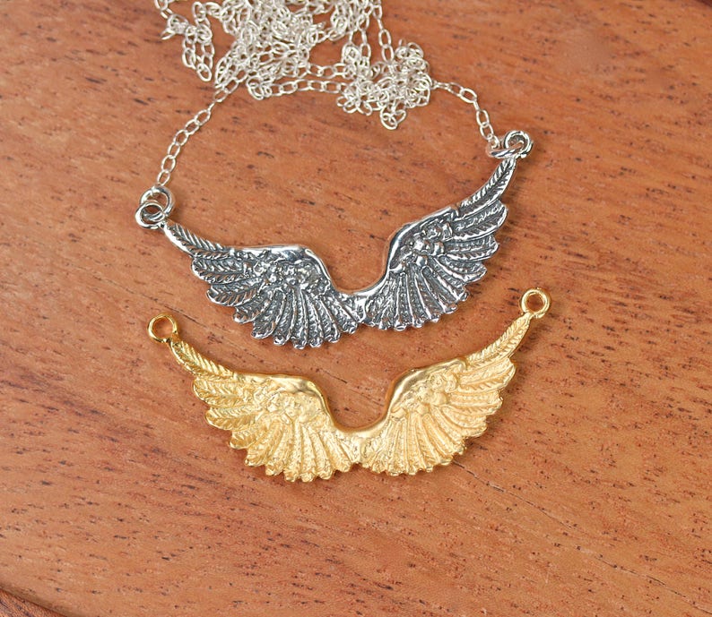 Peut inclure: Deux breloques d'ailes d'ange en argent, l'une sur un collier &agrave; cha&icirc;ne et l'autre sur une cha&icirc;ne s&eacute;par&eacute;e. Les ailes d'ange sont d&eacute;taill&eacute;es et ont une finition textur&eacute;e. Le collier est en argent et a une cha&icirc;ne d&eacute;licate.