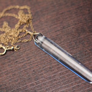 May include: A gold chain necklace with a clear crystal pendant shaped like a long, thin point.