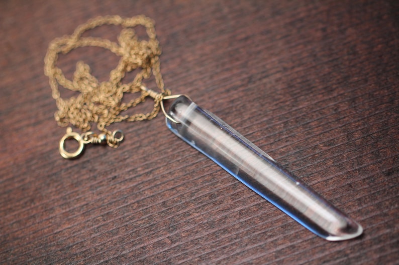 May include: A gold chain necklace with a clear crystal pendant shaped like a long, thin point.