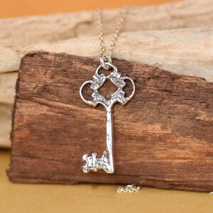 May include: Silver key pendant necklace with an ornate design. The key has a detailed, intricate design with a heart-shaped top and a long, slender shaft.