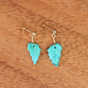 May include: A pair of turquoise leaf earrings with gold-toned posts and wire accents.
