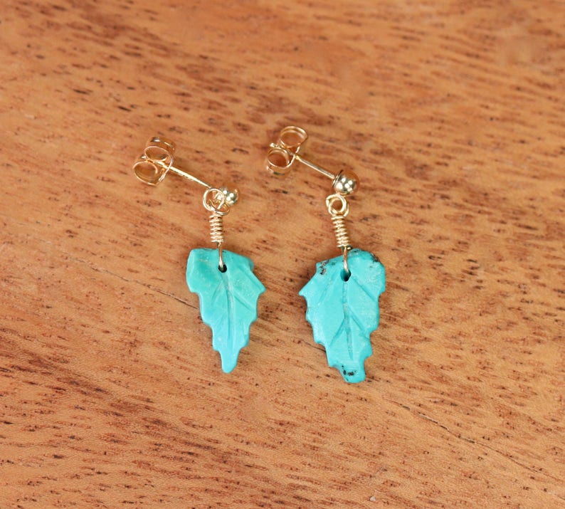 May include: A pair of turquoise leaf earrings with gold-toned posts and wire accents.
