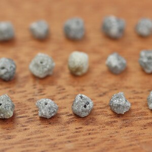 May include: A collection of 14 small, rough, grey diamonds on a wooden surface.