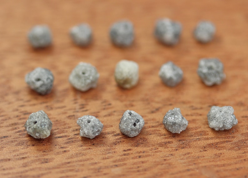 May include: A collection of 14 small, rough, grey diamonds on a wooden surface.