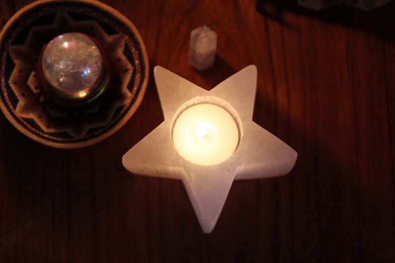 May include: A white star-shaped candle holder with a lit candle inside. The holder is made of a smooth, white material and has a slightly textured surface. The candle is a small, round, white candle.