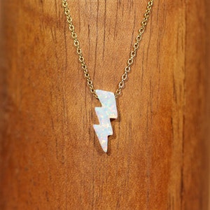 May include: A gold chain necklace with a white opal lightning bolt pendant.