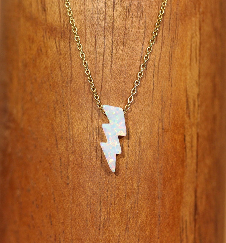 May include: A gold chain necklace with a white opal lightning bolt pendant.