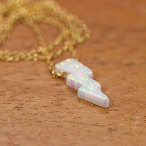 May include: A gold chain necklace with a white opal lightning bolt pendant.