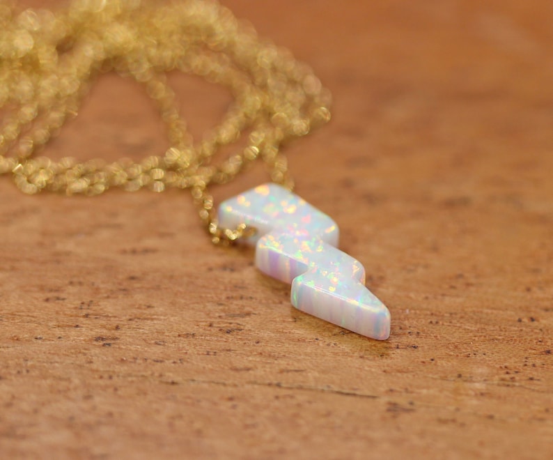 May include: A gold chain necklace with a white opal lightning bolt pendant.