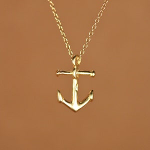 May include: A gold anchor pendant necklace. The anchor is a simple design with a rounded top and a slightly curved bottom.