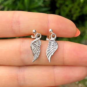 May include: A pair of silver earrings with a wing design. The wings are detailed and have a textured finish.