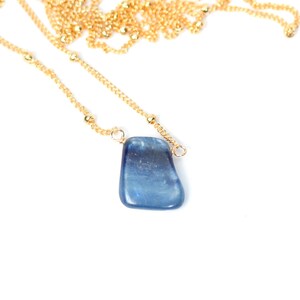 May include: A gold chain necklace with a blue gemstone pendant. The pendant is a freeform shape and has a light blue color.