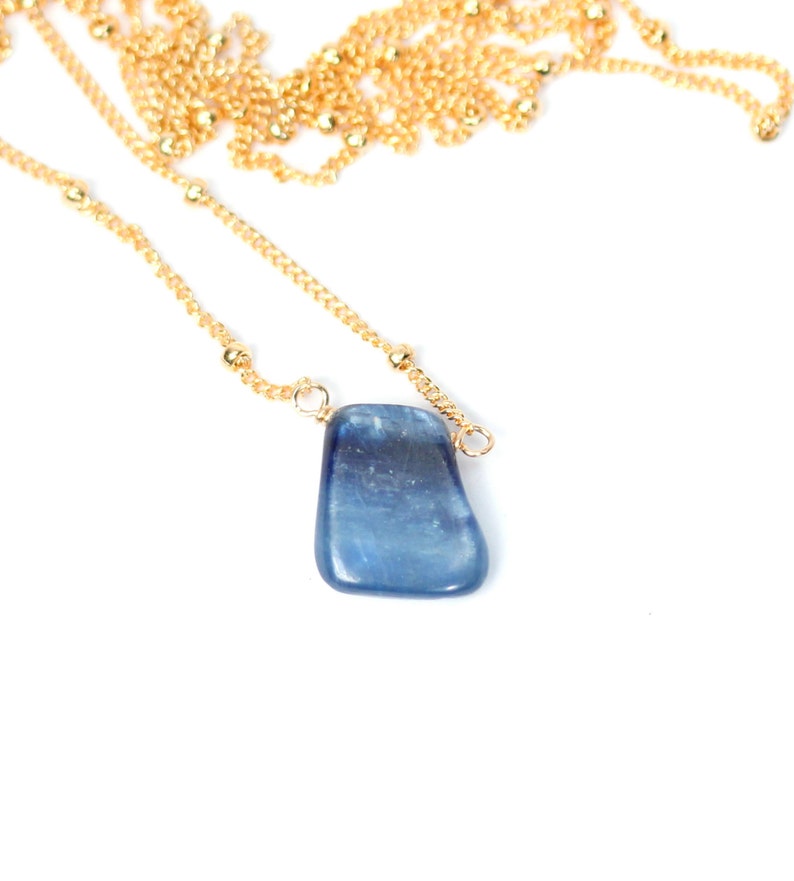 May include: A gold chain necklace with a blue gemstone pendant. The pendant is a freeform shape and has a light blue color.