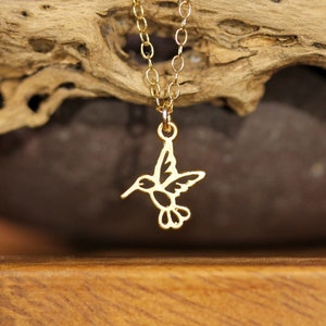 May include: A gold hummingbird necklace with a delicate chain. The hummingbird pendant is cut out and has a detailed design.