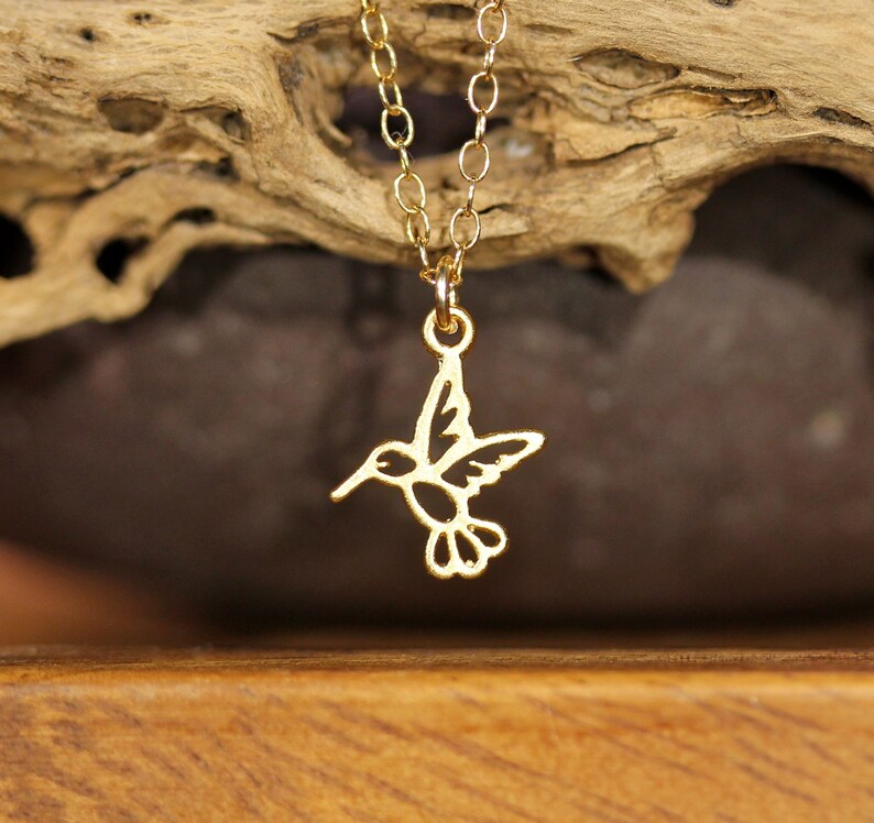May include: A gold hummingbird necklace with a delicate chain. The hummingbird pendant is cut out and has a detailed design.