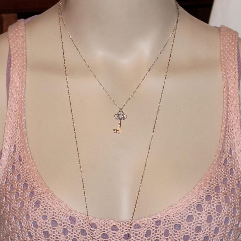 May include: A gold key pendant necklace with a delicate chain. The key has a detailed design and is accented with small sparkling stones.