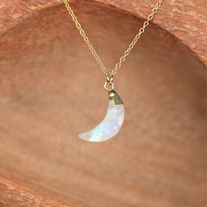 May include: A gold chain necklace with a crescent moon pendant made of iridescent moonstone.