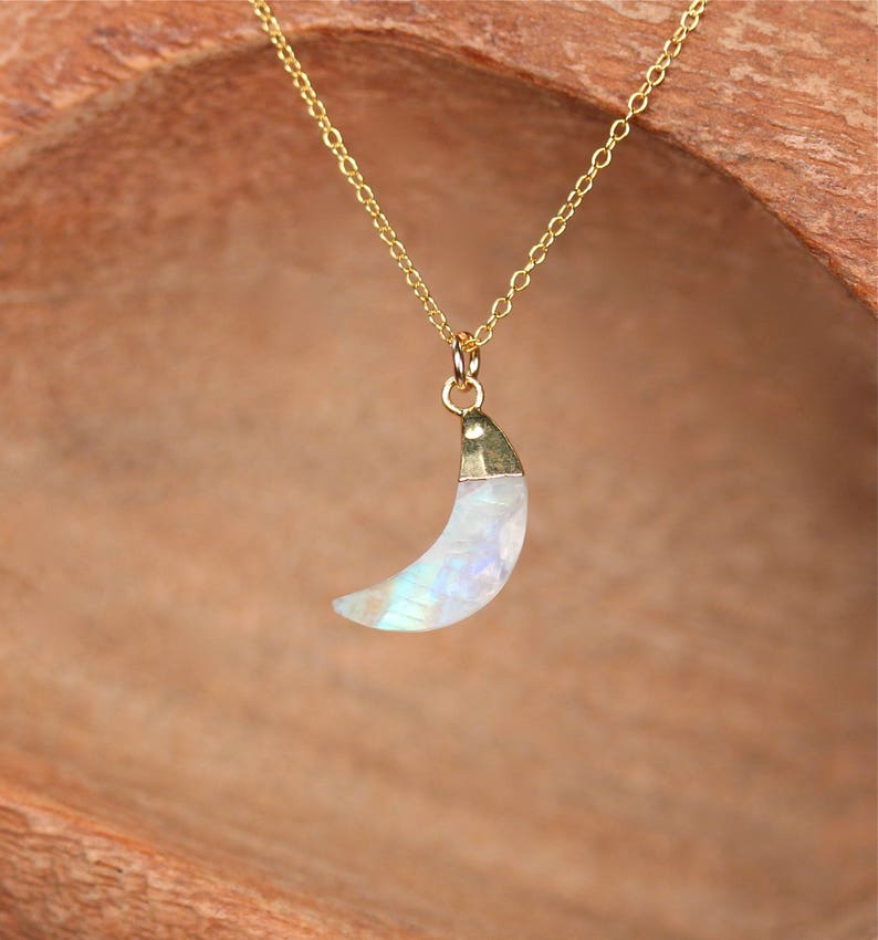 May include: A gold chain necklace with a crescent moon pendant made of iridescent moonstone.