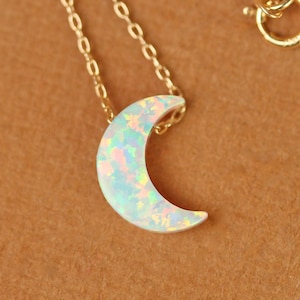 May include: A gold chain necklace with a crescent moon pendant made of iridescent opal.