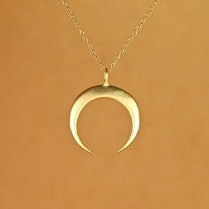 Può includere: Una collana con un ciondolo a forma di mezzaluna d'oro. Il ciondolo è un design semplice e minimalista con una finitura liscia e lucida.