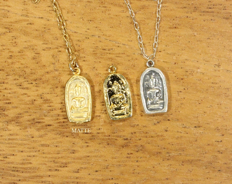 May include: Three gold and silver necklaces with pendants featuring a Buddha figure. The pendants are rectangular and have a matte finish.