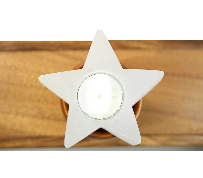 May include: A white ceramic star-shaped candle holder with a round opening for a tea light. The holder is sitting on a wooden surface.