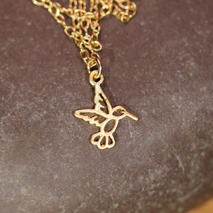 May include: A gold chain necklace with a delicate hummingbird pendant. The hummingbird is cut out of metal and has a detailed design.