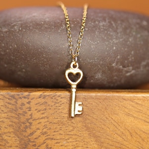 Puede incluir: Un collar de oro con una llave en forma de coraz&oacute;n. El collar est&aacute; sobre una superficie de madera marr&oacute;n.
