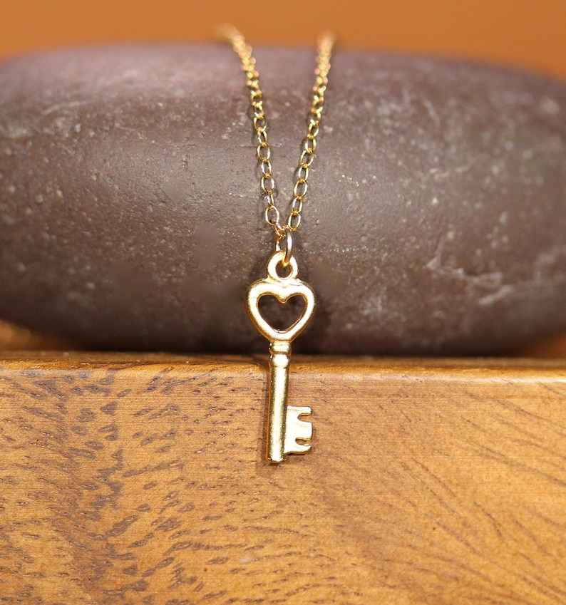 Puede incluir: Un collar de oro con una llave en forma de coraz&oacute;n. El collar est&aacute; sobre una superficie de madera marr&oacute;n.