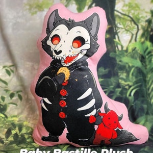 May include: A pink plush pillow with a black and white wolf character wearing a black and white skeleton costume. The wolf is holding a red and white toy devil in its right hand. The text "Baby Bastille Plush Pillow!" is at the bottom of the image.
