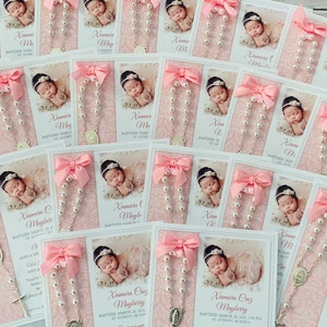 May include: Pink and white baptism favors with a photo of a baby girl, a silver rosary, and a pink ribbon. The card reads "Xiamara Cruz Mayberry Baptized March 28, 2021, 1:00 PM St. Anthony de Padua"