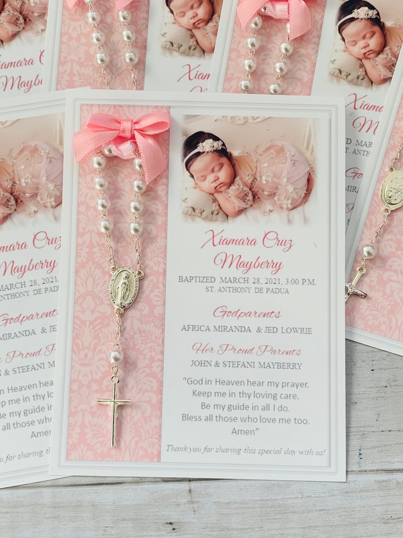 May include: A white card with pink trim and a pink bow. The card has a picture of a baby girl on it. The text on the card reads "Xiamara Cruz Mayberry Baptized March 28, 2021, 3:00 PM. St. Anthony de Padua Godparents Africa Miranda & Jed Lowrie Her Proud Parents John & Stefani Mayberry "God in Heaven hear my prayer. Keep me in thy loving care. Be my guide in all I do. Bless all those who love me too. Amen" Thank you for sharing this special day with us!"