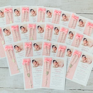 May include: Pink and white cards with a photo of a baby and a small rosary with a silver charm. The cards have the text "Anamara Grace" and "Baptized into the Love of God" on them.