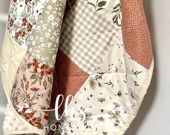 Puede incluir: Un edredón patchwork con una variedad de patrones florales y geométricos en tonos crema, beige y rojo apagado. El edredón presenta estampados florales, cuadros vichy y lunares, con una textura acolchada.
