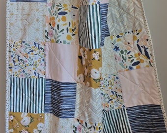 Puede incluir: Un edredón de patchwork con una variedad de patrones, incluyendo diseños florales, a rayas y geométricos en tonos rosa, dorado, azul marino y blanco. El edredón tiene un borde punteado y el texto "lhs LITTLE HOMEMADE SHOP".