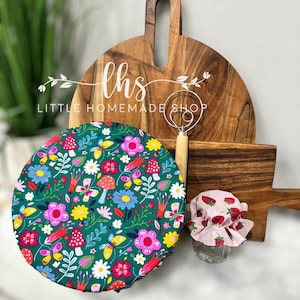 May include: A set of two green and white fabric bowl covers with a floral and butterfly design. The covers are on a wooden chopping board with the text "lhs LITTLE HOMEMADE SHOP".