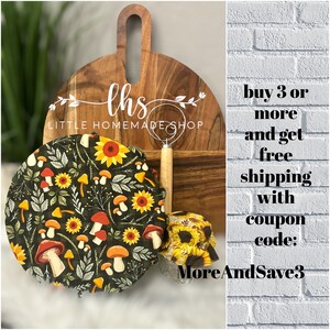 Può includere: Tre coperchi per ciotole in tessuto con un motivo a funghi e girasoli. I coperchi sono su un tagliere di legno con un cartello che dice "ths LITTLE HOMEMADE SHOP". Il testo "buy 3 or more and get free shipping with coupon code: MoreAndSave3" è su uno sfondo di mattoni bianchi.
