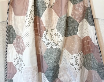 May include: A patchwork quilt with a hexagonal pattern in shades of pink, gray, and white. The quilt features a variety of patterns, including floral, polka dot, and leaf designs. The quilt is edged with a black and white striped trim.