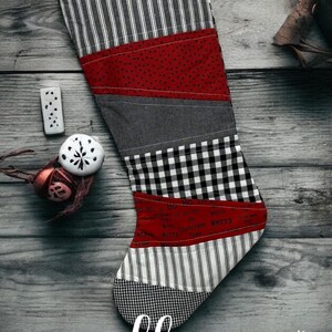May include: A red, black, white, and gray patchwork Christmas stocking with the text "Ho Ho Ho" and "Merry Christmas" on it. The stocking is hanging on a wooden surface.