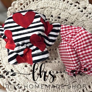 May include: Two fabric face masks with red and white patterns. The first mask has black and white stripes with red hearts. The second mask has a red and white gingham pattern. The masks are on a crocheted doily. The text "lhs LITTLE HOMEMADE SHOP" is visible at the bottom of the image.